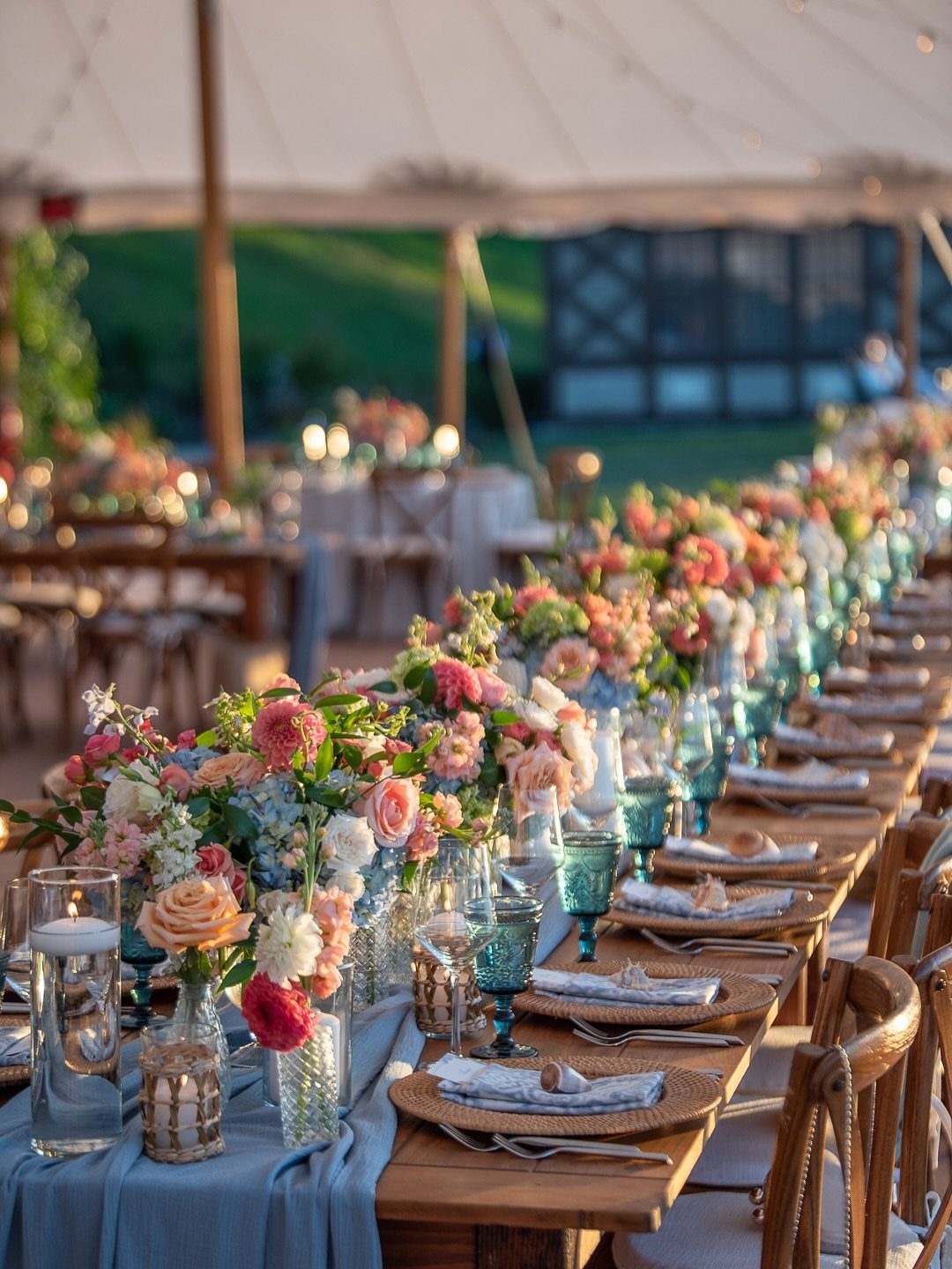 Wedding table with light blue runner, blue glasses, and colorful floral centerpieces.