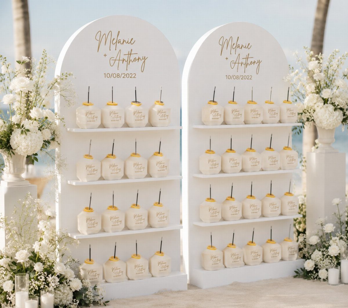 White arched paleta stands with frozen treats and white flowers on a beach.