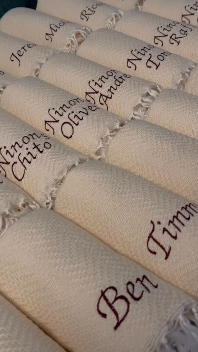 Rolled cream beach towels with personalized names embroidered in dark brown cursive script.