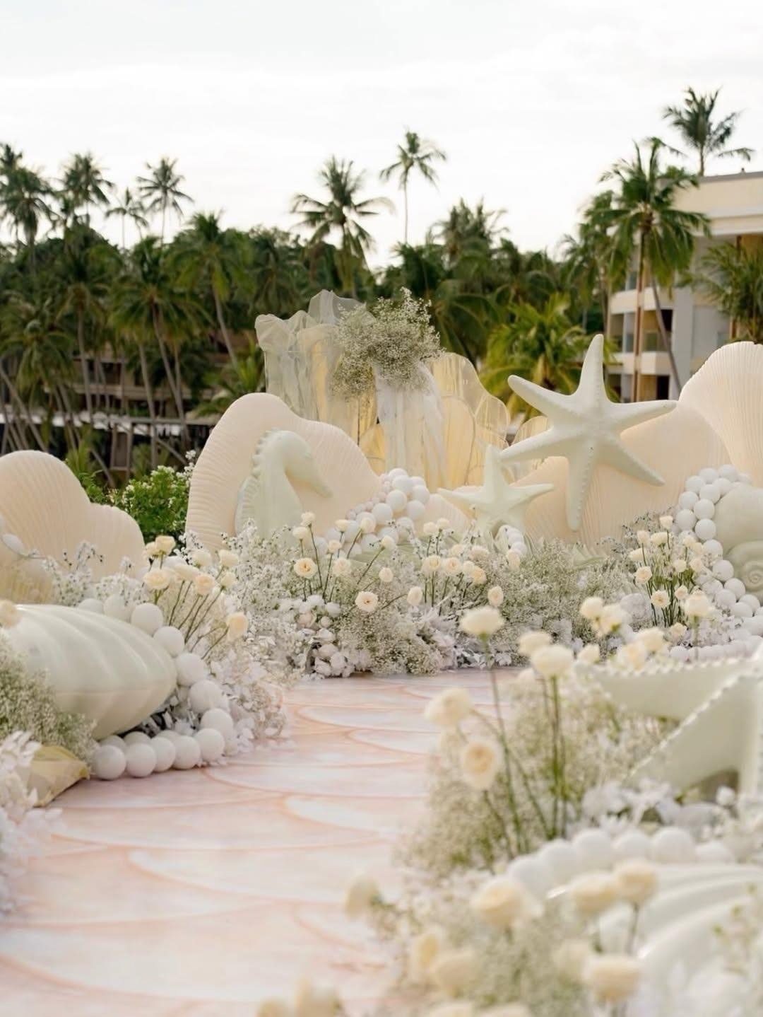 Giant white seashells and starfish decorating a floral wedding aisle with palm trees.