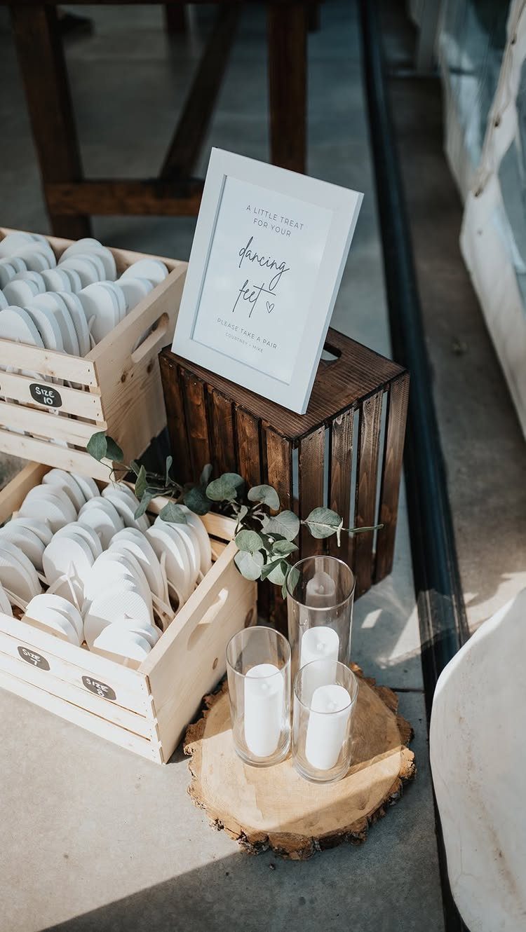 White flip-flops in wooden crates with a sign and candles for guests.