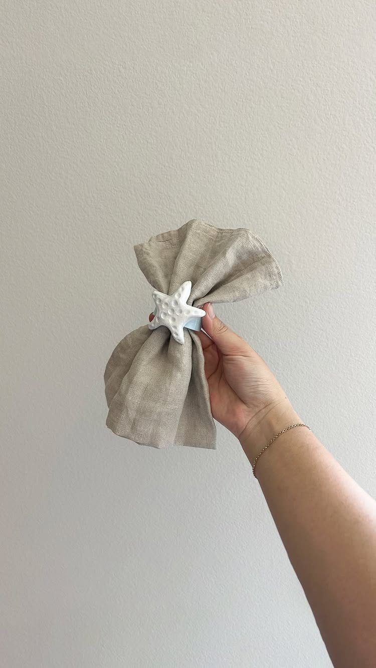 Beige linen napkin held by a hand with a white starfish napkin ring.