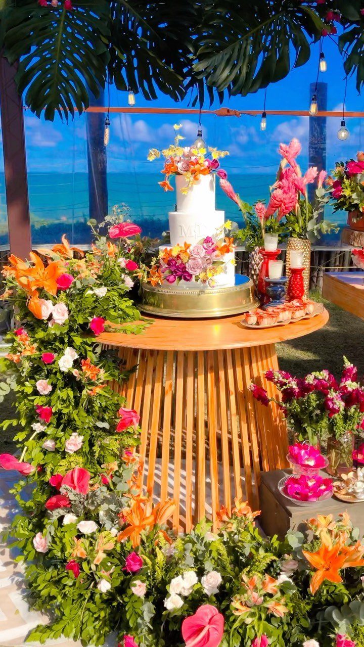 White tiered wedding cake with tropical flowers on a wooden table by the ocean