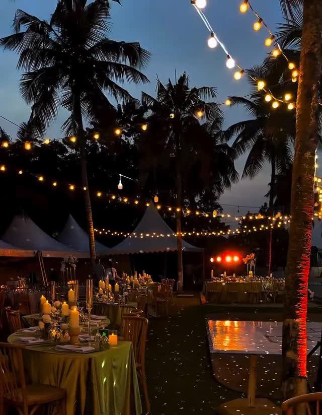 Outdoor evening wedding reception with green tablecloths, candles, and string lights under palm trees.
