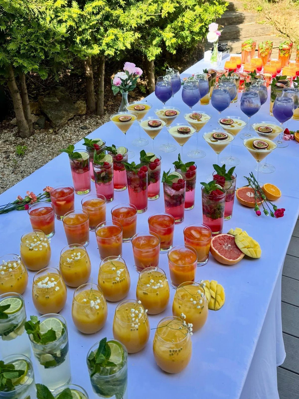 Colorful tropical cocktails with fruit garnishes arranged on a white outdoor table.
