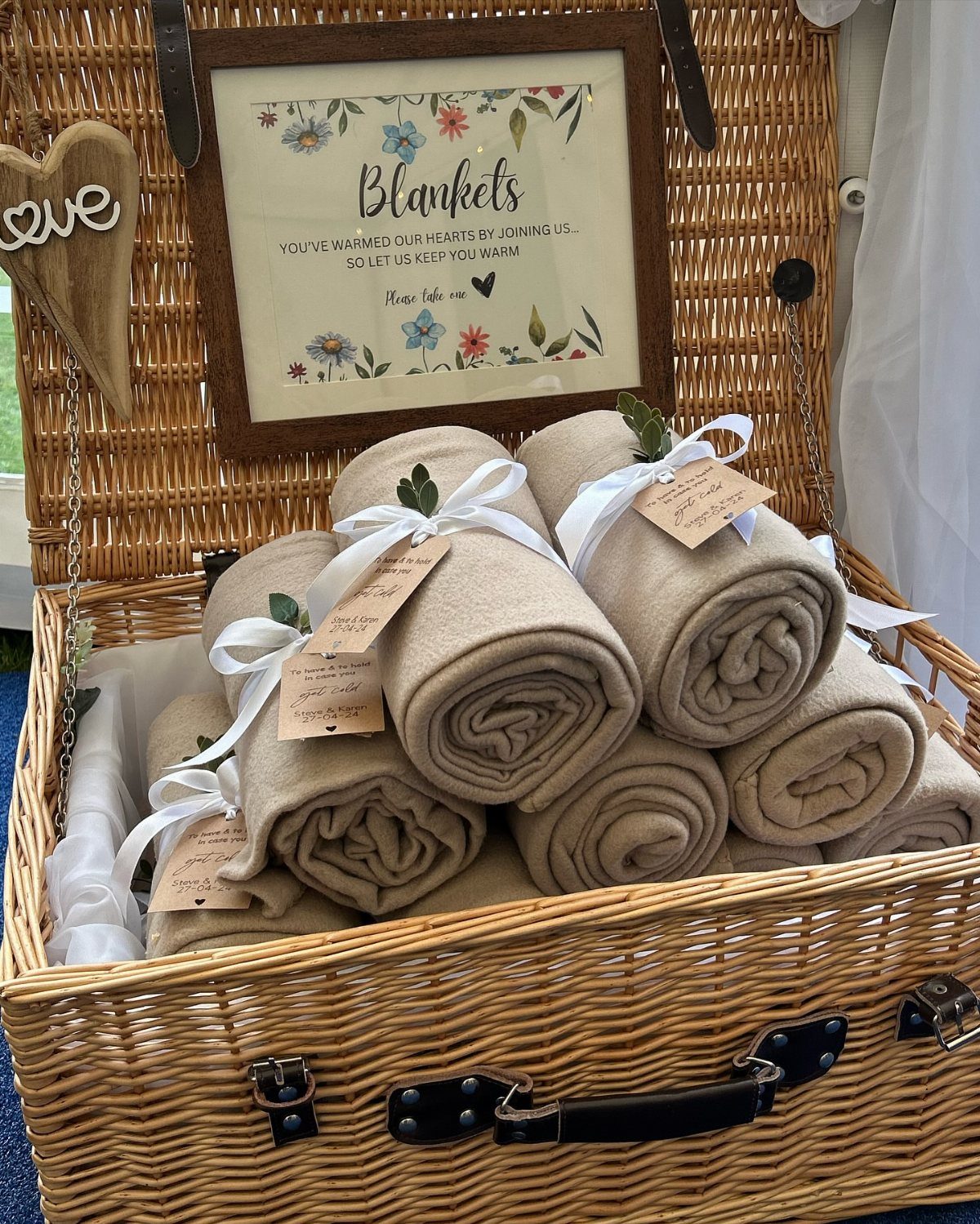 Rolled beige blankets with white ribbons inside a large woven wicker basket.