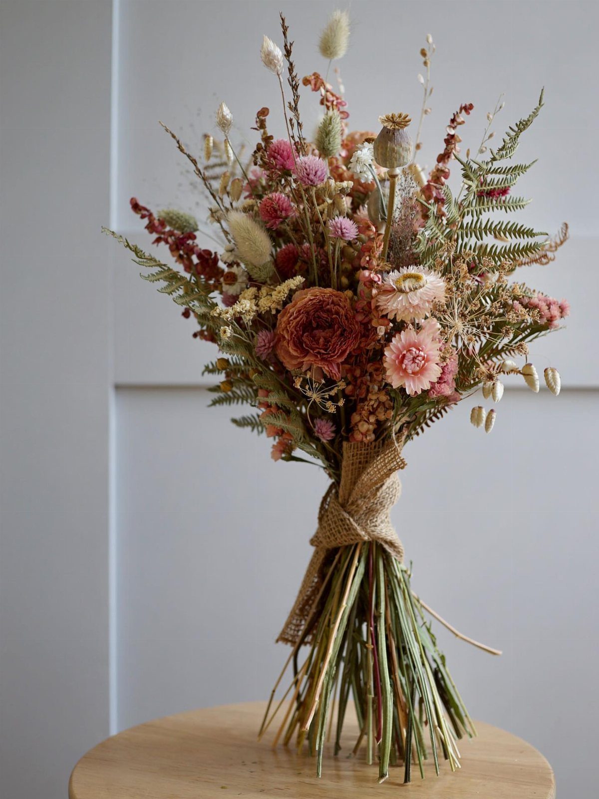Dried flower bouquet with terracotta blooms and fronds tied with burlap ribbon.