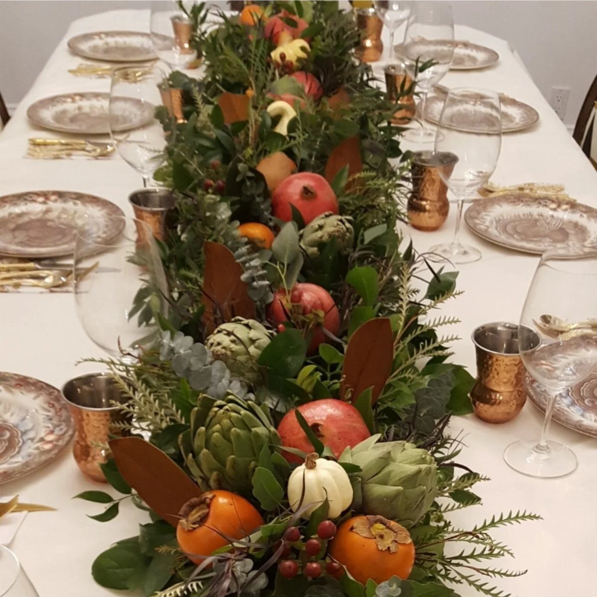 Table centerpiece featuring pomegranates, persimmons, and greenery on a white wedding table.