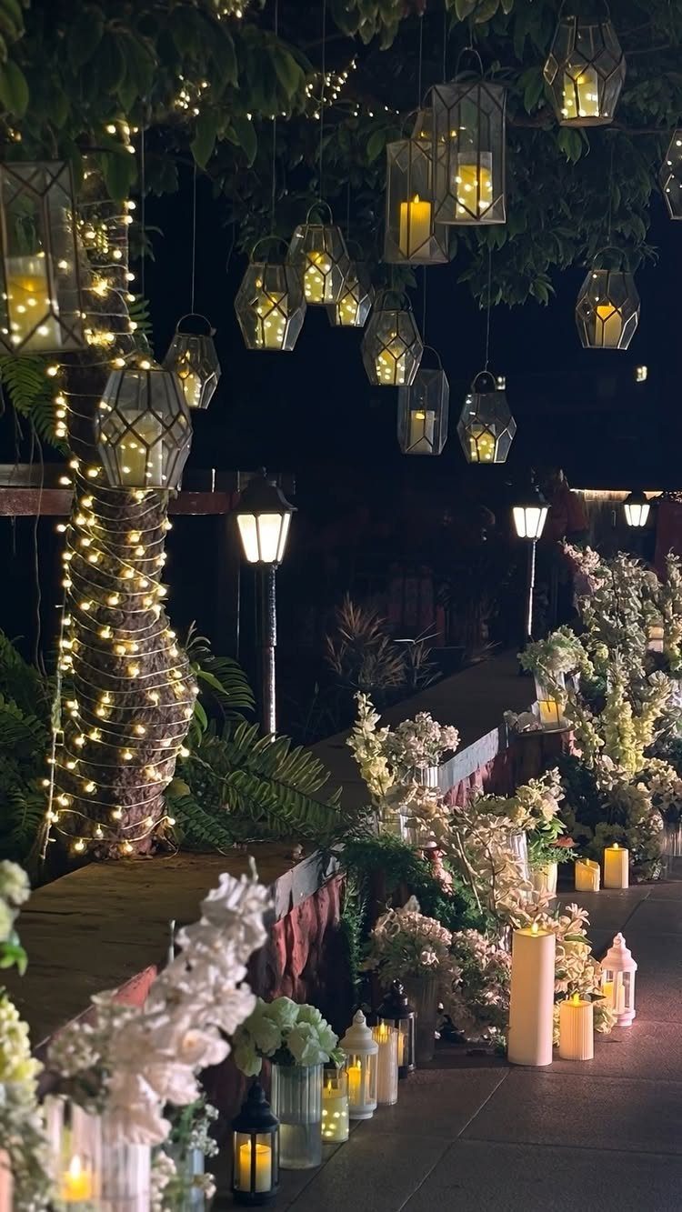Tree wrapped in fairy lights with hanging lanterns and white floral walkway decorations
