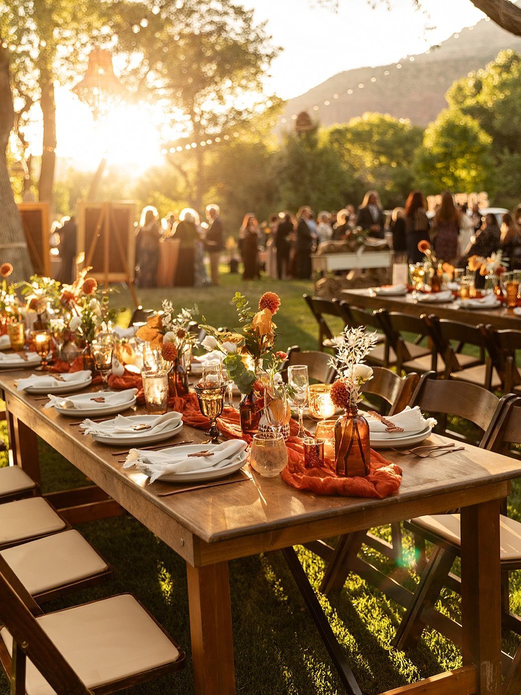 Wooden wedding tables set with orange runners and autumn florals at sunset.