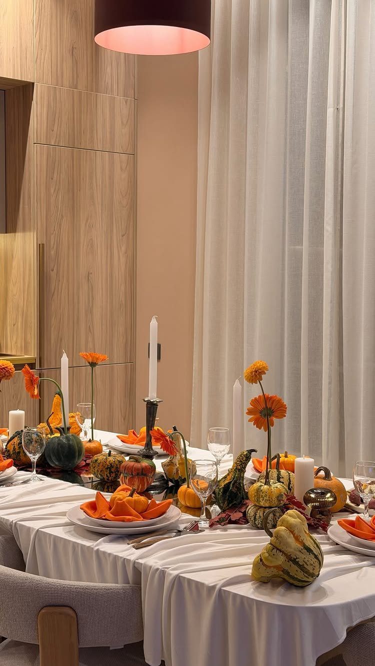 Dining table decorated with orange flowers, pumpkins, and white candles for autumn.
