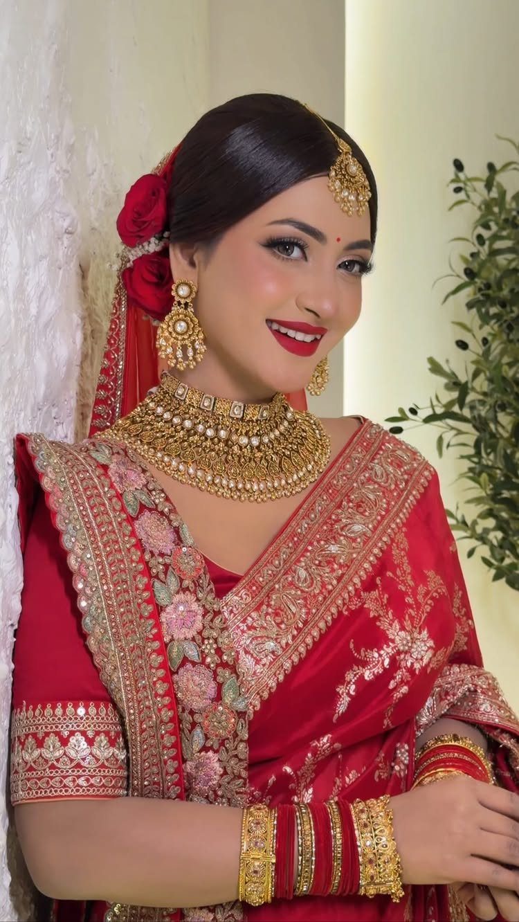 Woman in red bridal saree with gold jewelry and bold red lipstick.