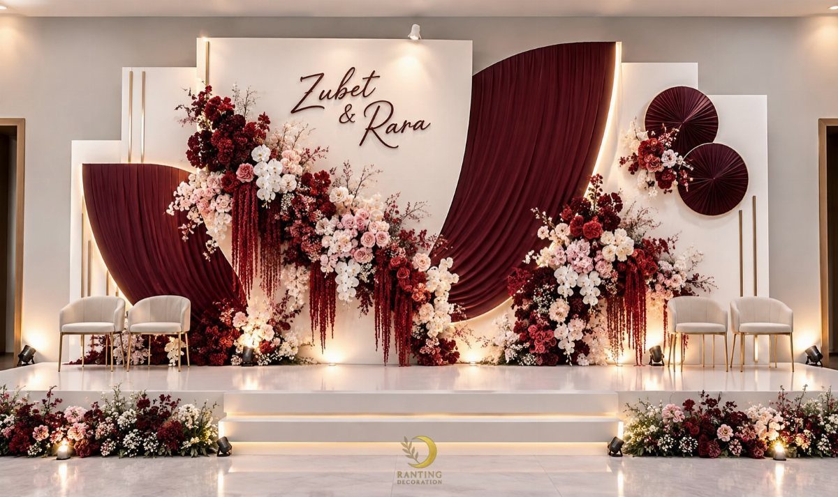Wedding stage backdrop with red draped fabric and lush red and pink floral arrangements.