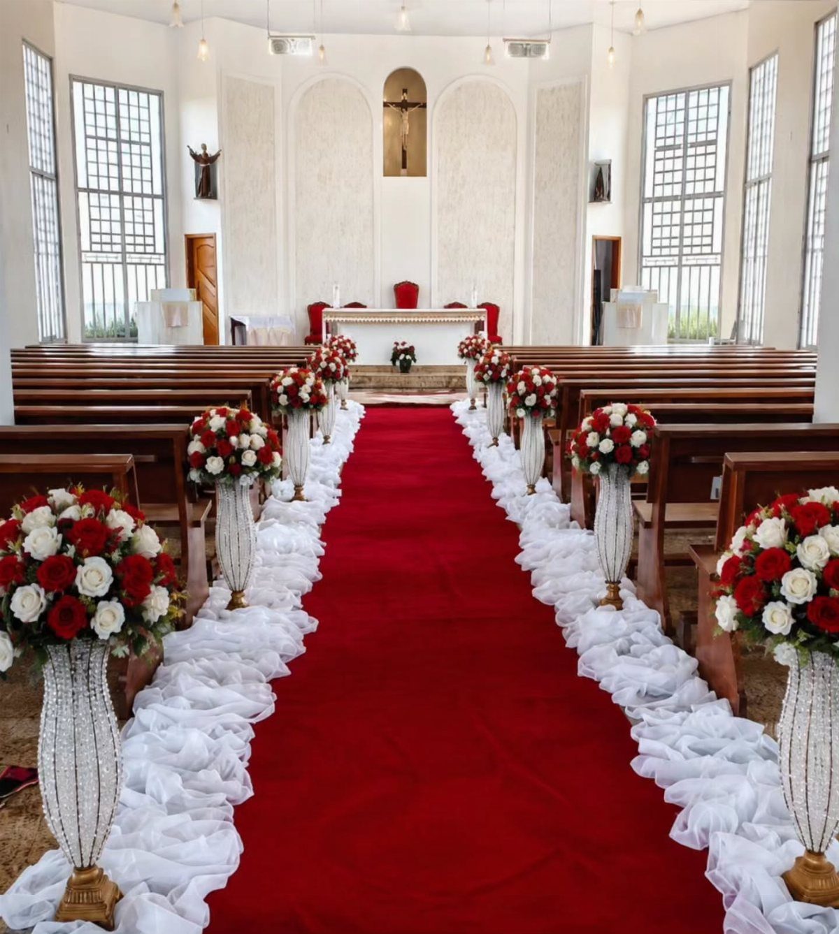 Red carpet aisle runner lined with white ruffles and red rose bouquets in church