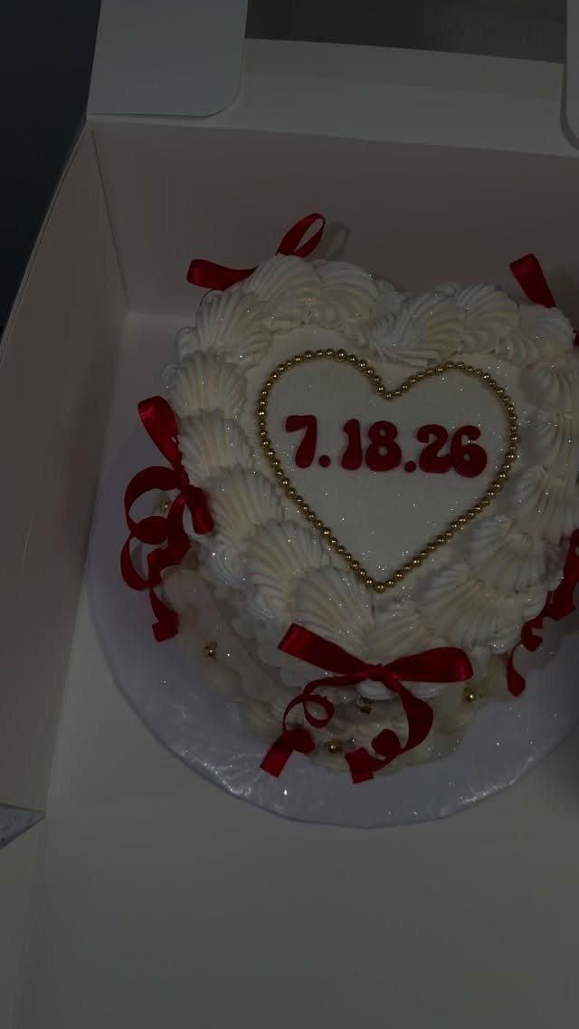 Heart-shaped white cake with red ribbons and a red date in the center.