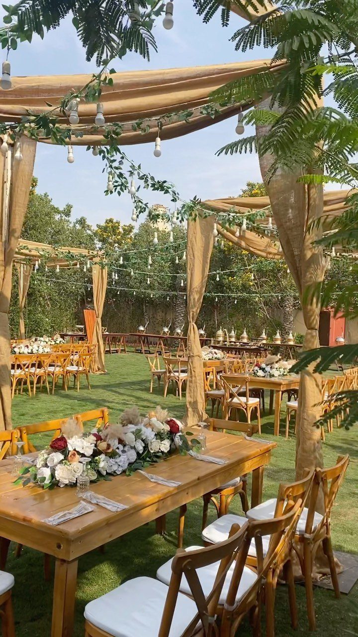 Wooden wedding tables with white flowers under beige fabric canopies on a lawn