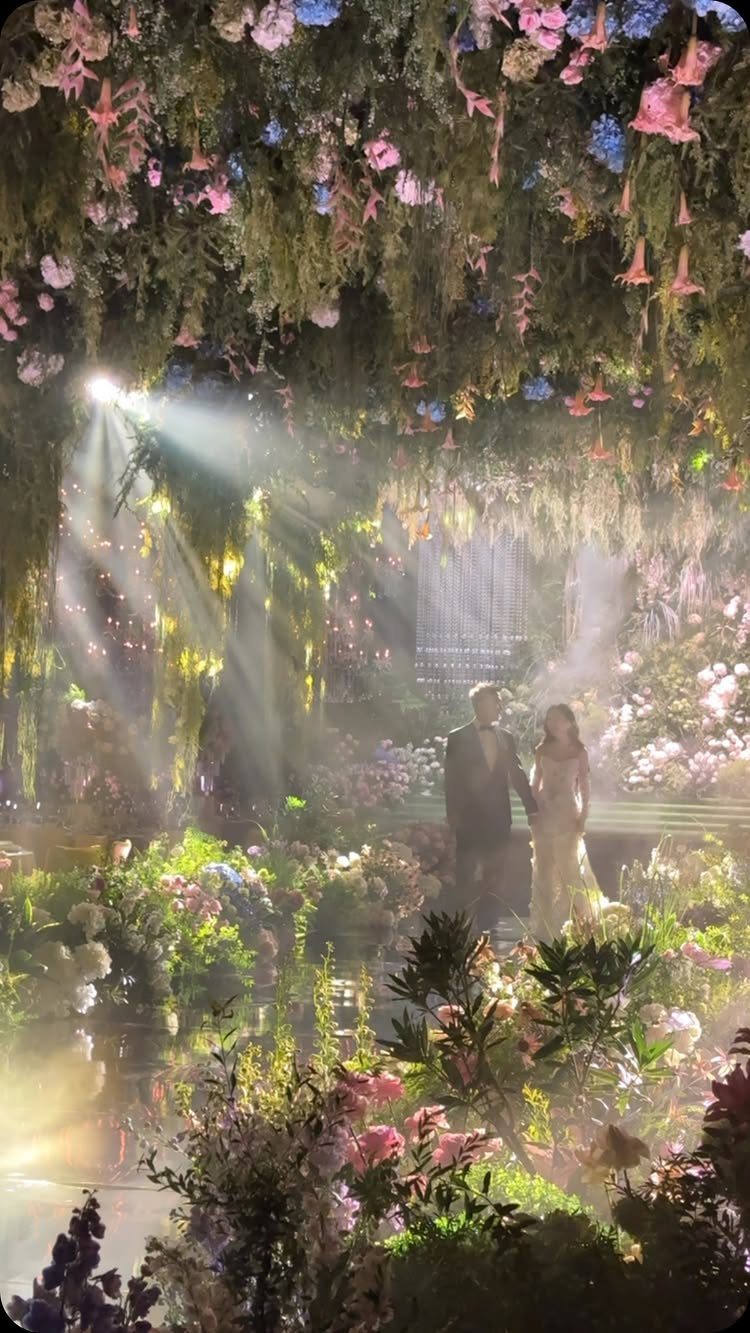 Wedding couple standing in a magical indoor garden with hanging flowers and light beams