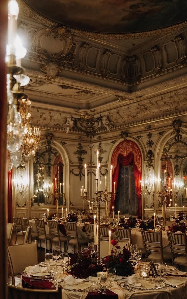 Opulent ballroom with gold moldings, red velvet curtains, and candlelit wedding tables.