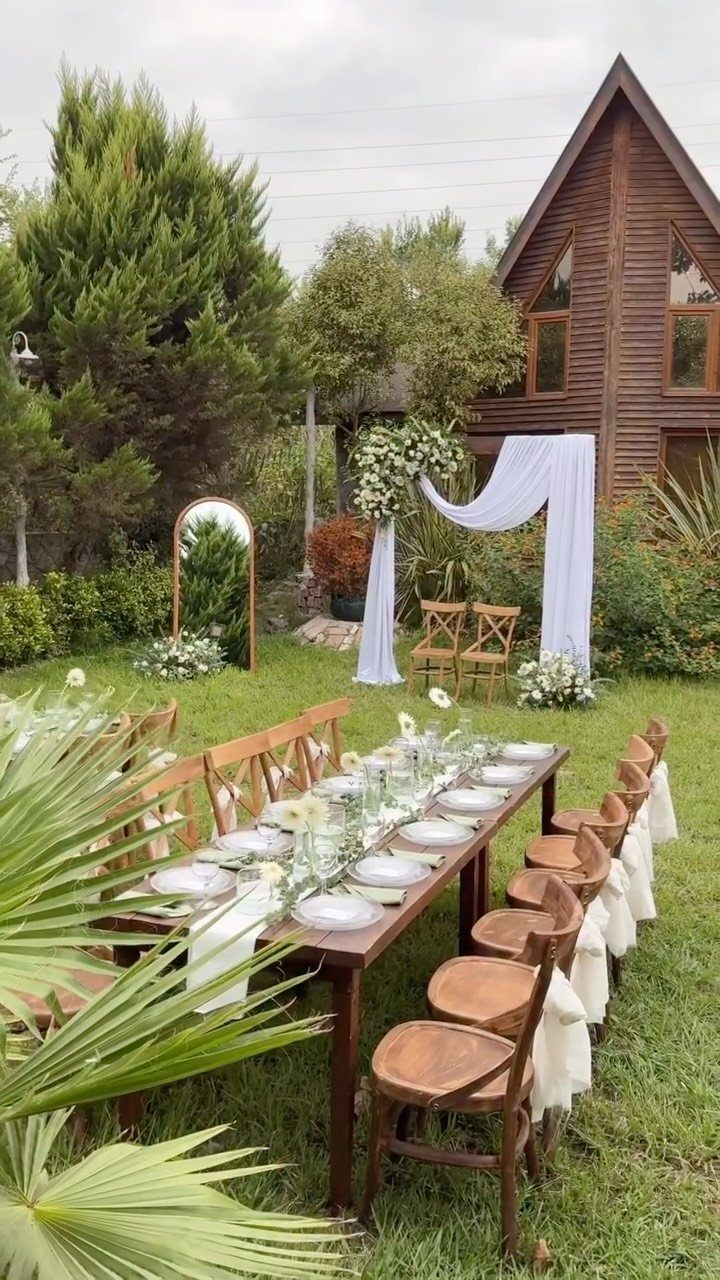 Wooden wedding table set on a green lawn with a floral white arch.