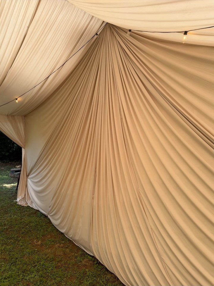 Cream draped fabric lining a tent ceiling with warm string lights.