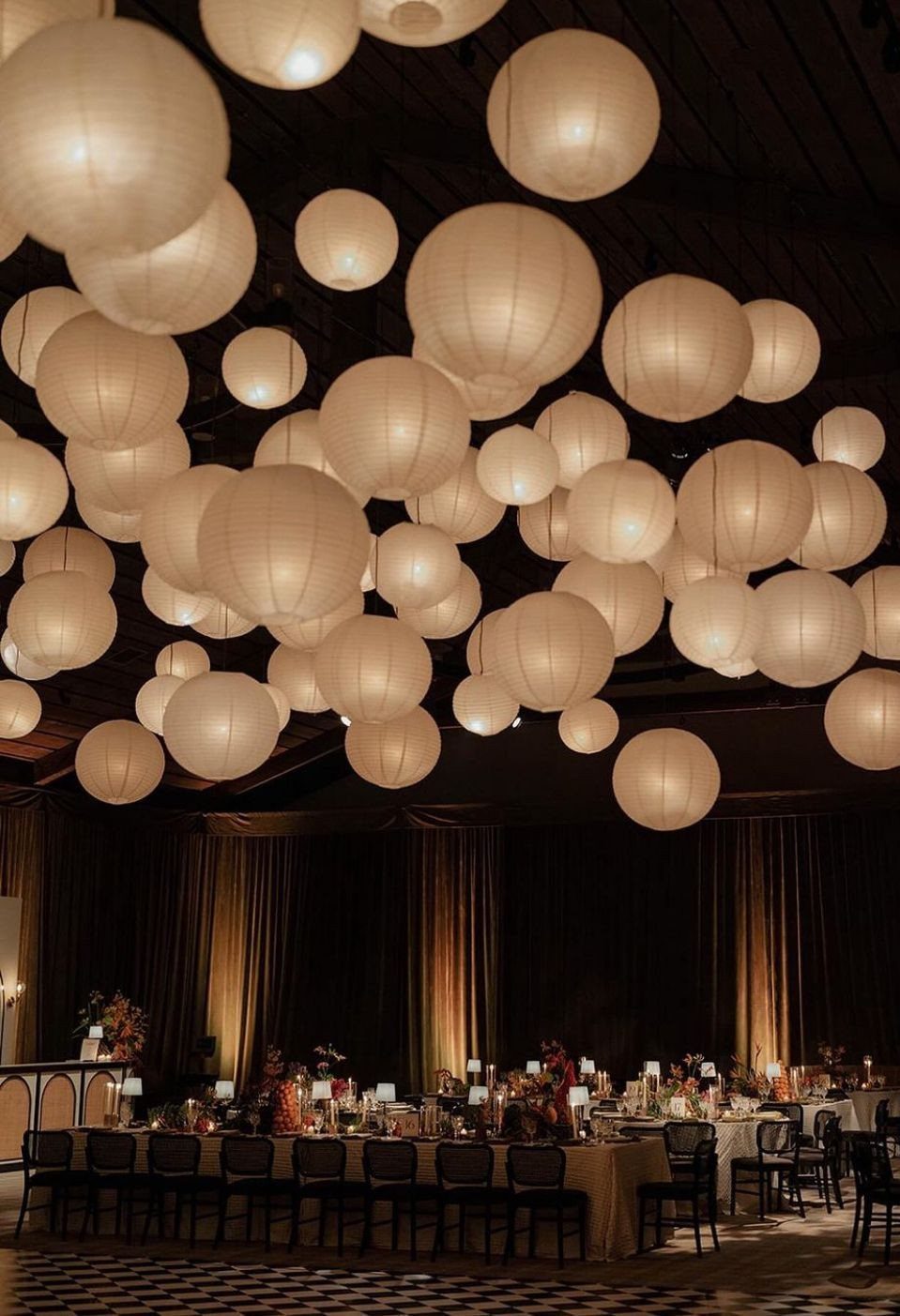 White spherical paper lanterns hanging over a long wedding banquet table in a hall.