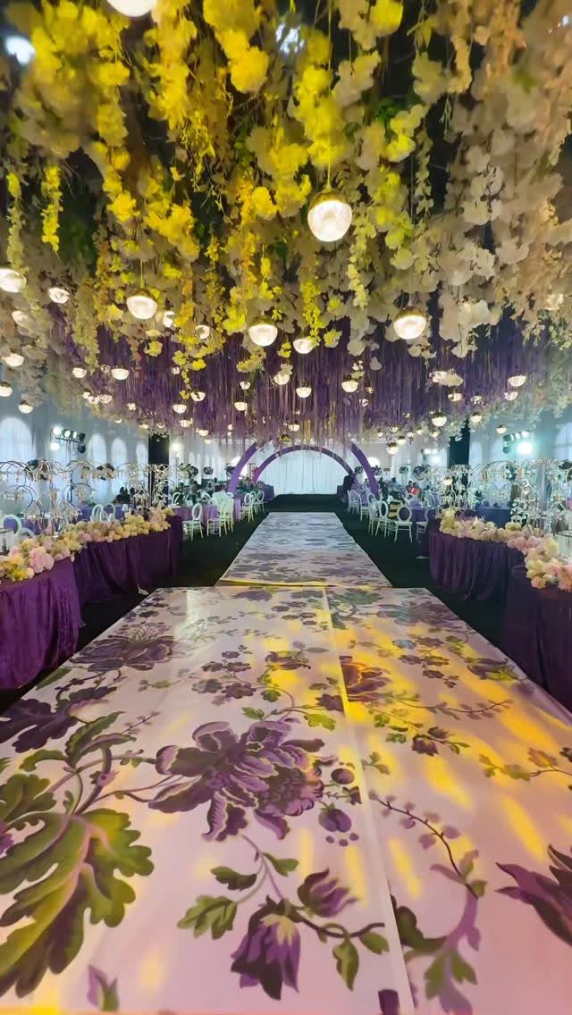 Wedding venue with yellow floral ceiling, glowing orb lights, and purple floral aisle.