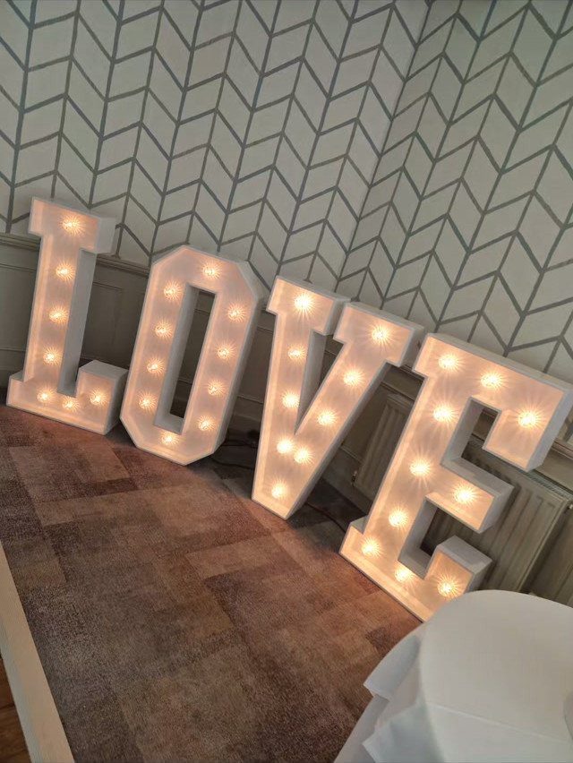Large white marquee letters spelling LOVE with glowing light bulbs on a floor