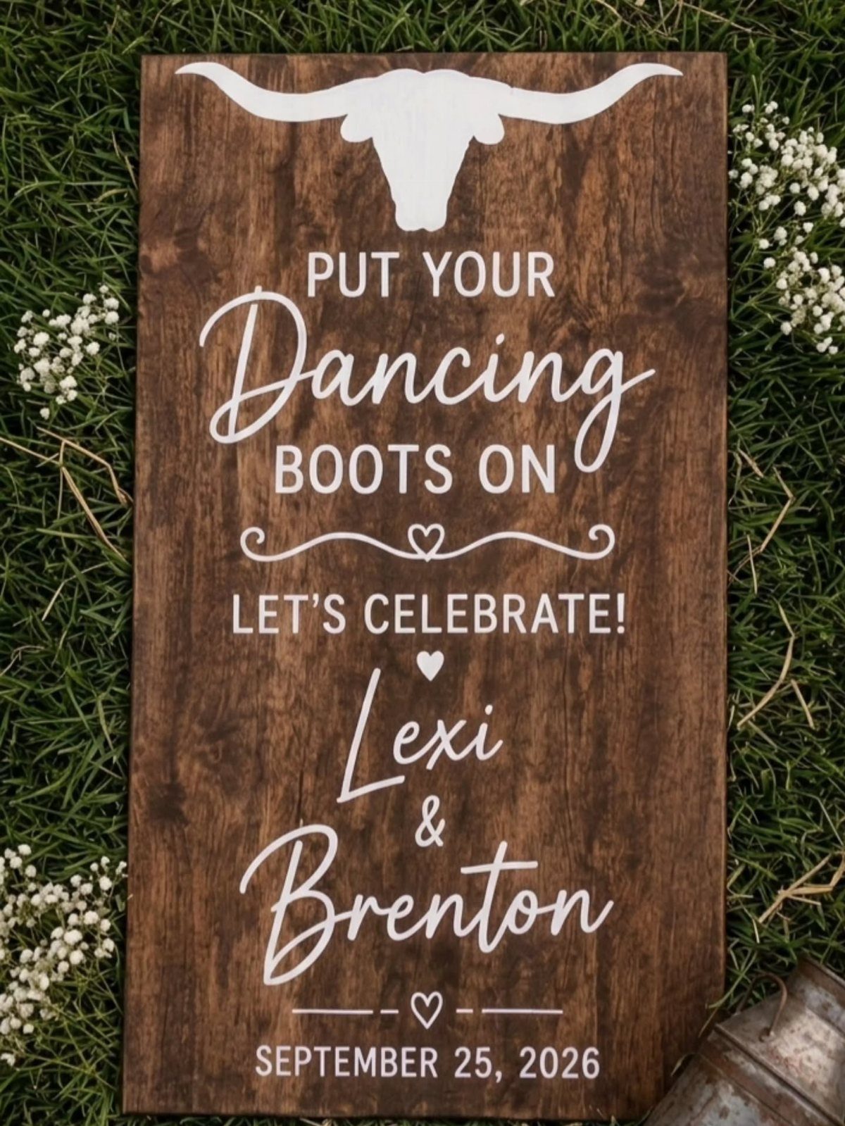 Wooden wedding sign with longhorn skull and white text resting on green grass