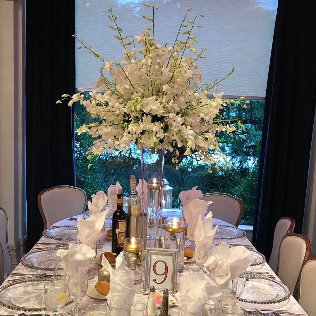 White orchid centerpiece in a glass vase on a formal wedding dinner table.