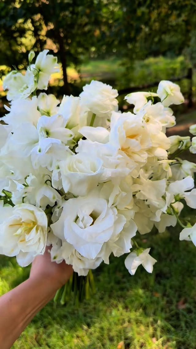 White lisianthus bouquet held by a hand against a blurred green garden background