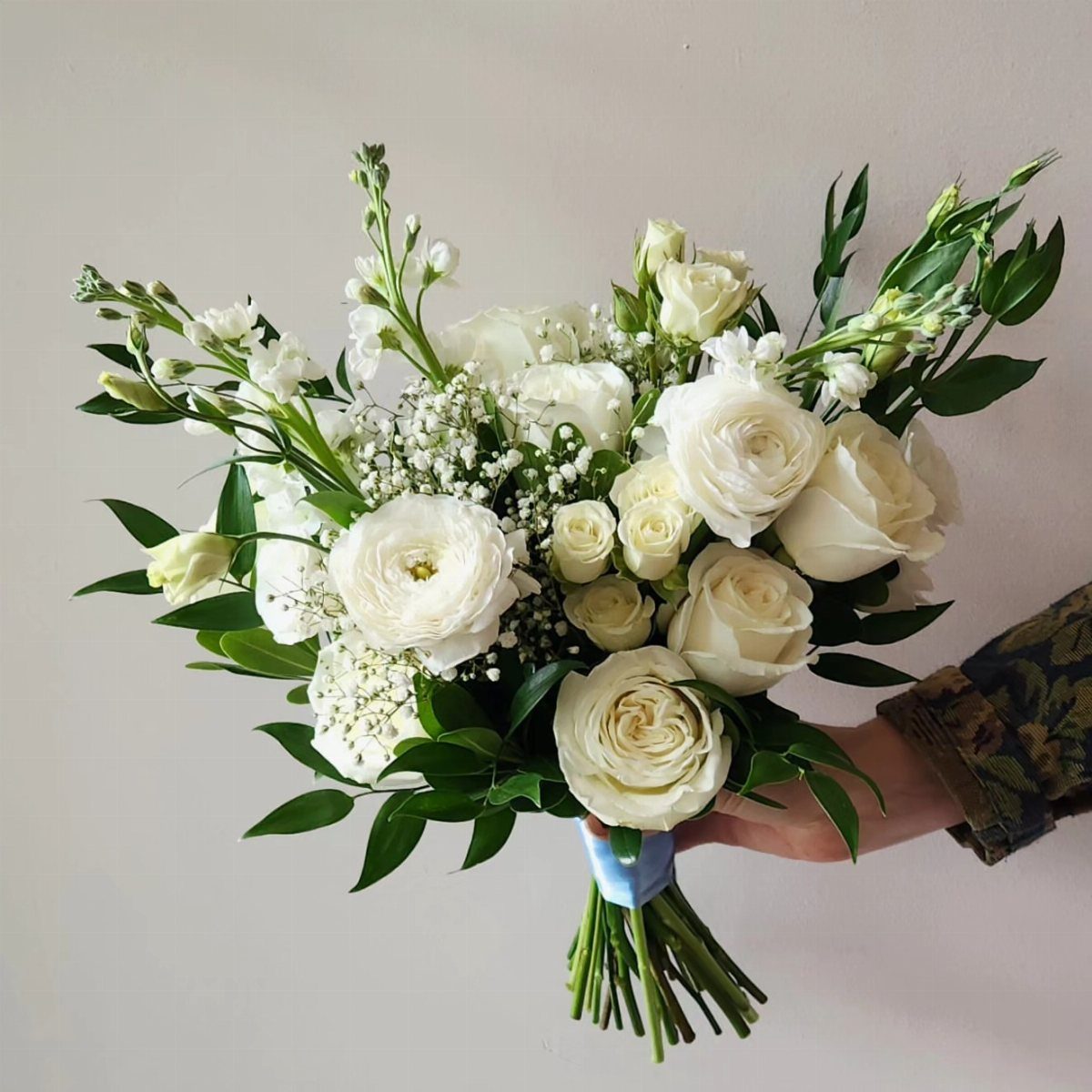 White bridal bouquet featuring ranunculus, roses, and baby's breath with green foliage.