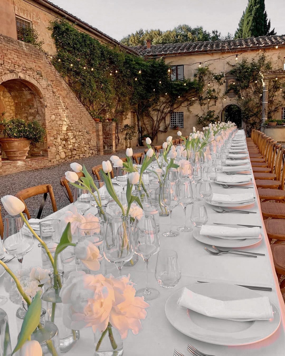 White tulips in small glass vases lining a long white wedding reception table.