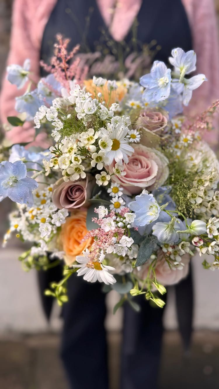 Colorful wildflower bridal bouquet with blue, pink, and orange flowers held by a person.