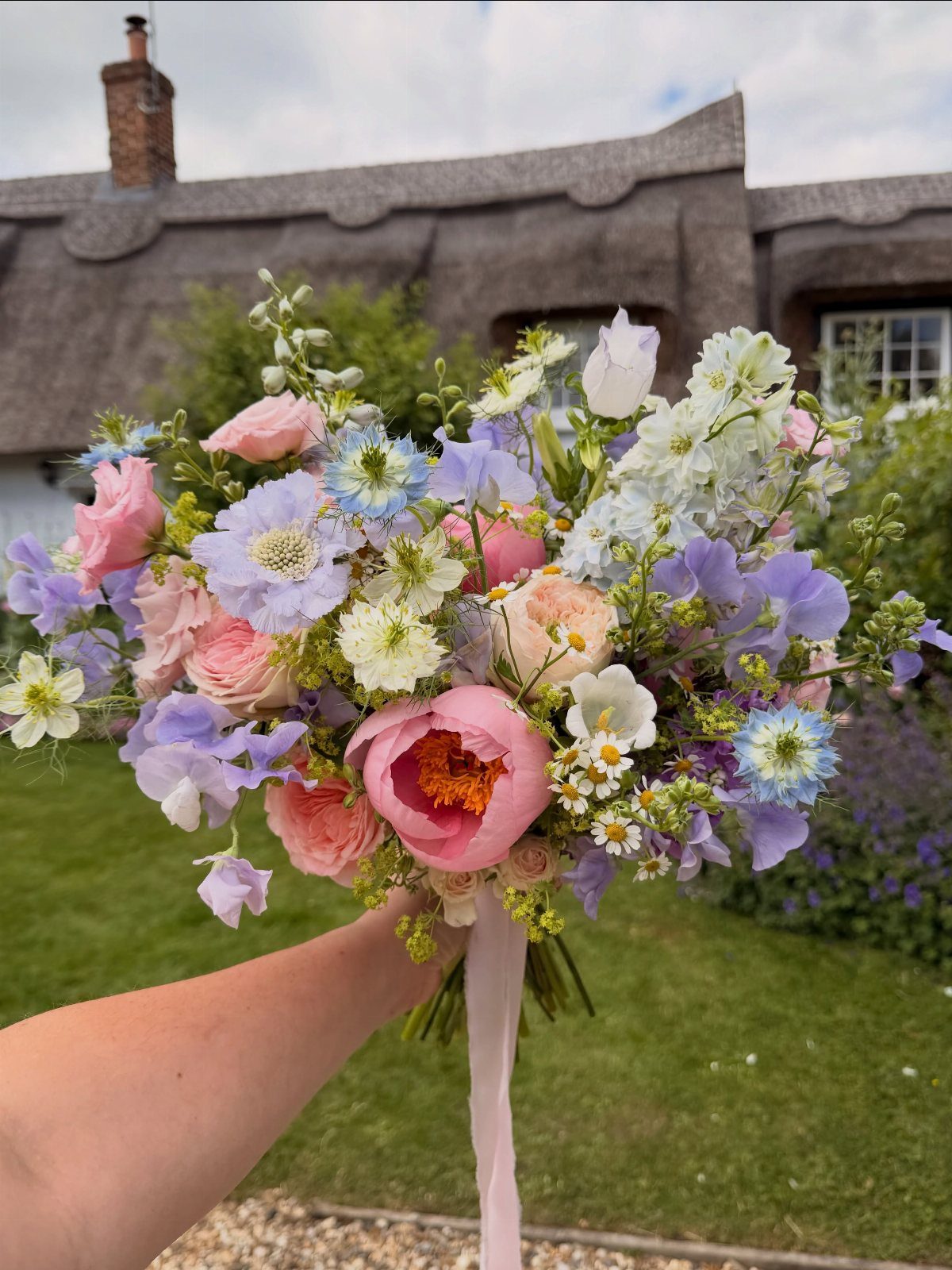 Colorful bridal bouquet with pink roses and blue scabiosa flowers held outdoors.