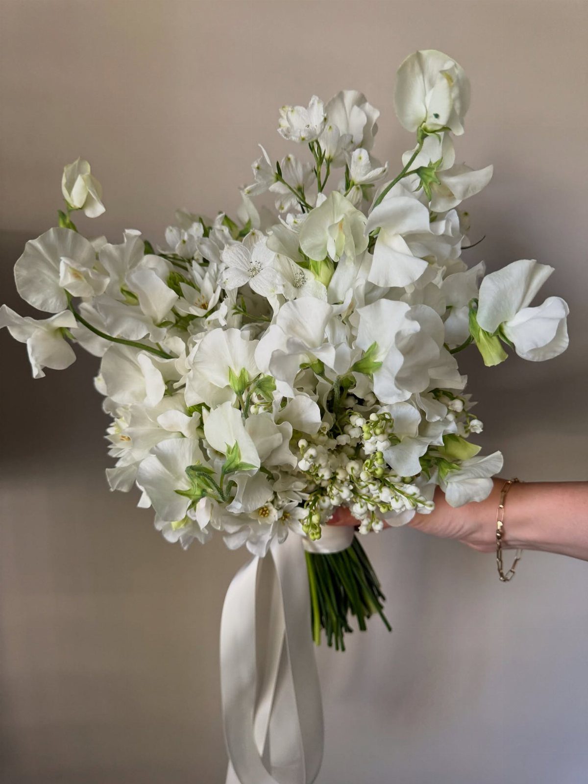 White sweet pea bridal bouquet tied with a white satin ribbon held by hand