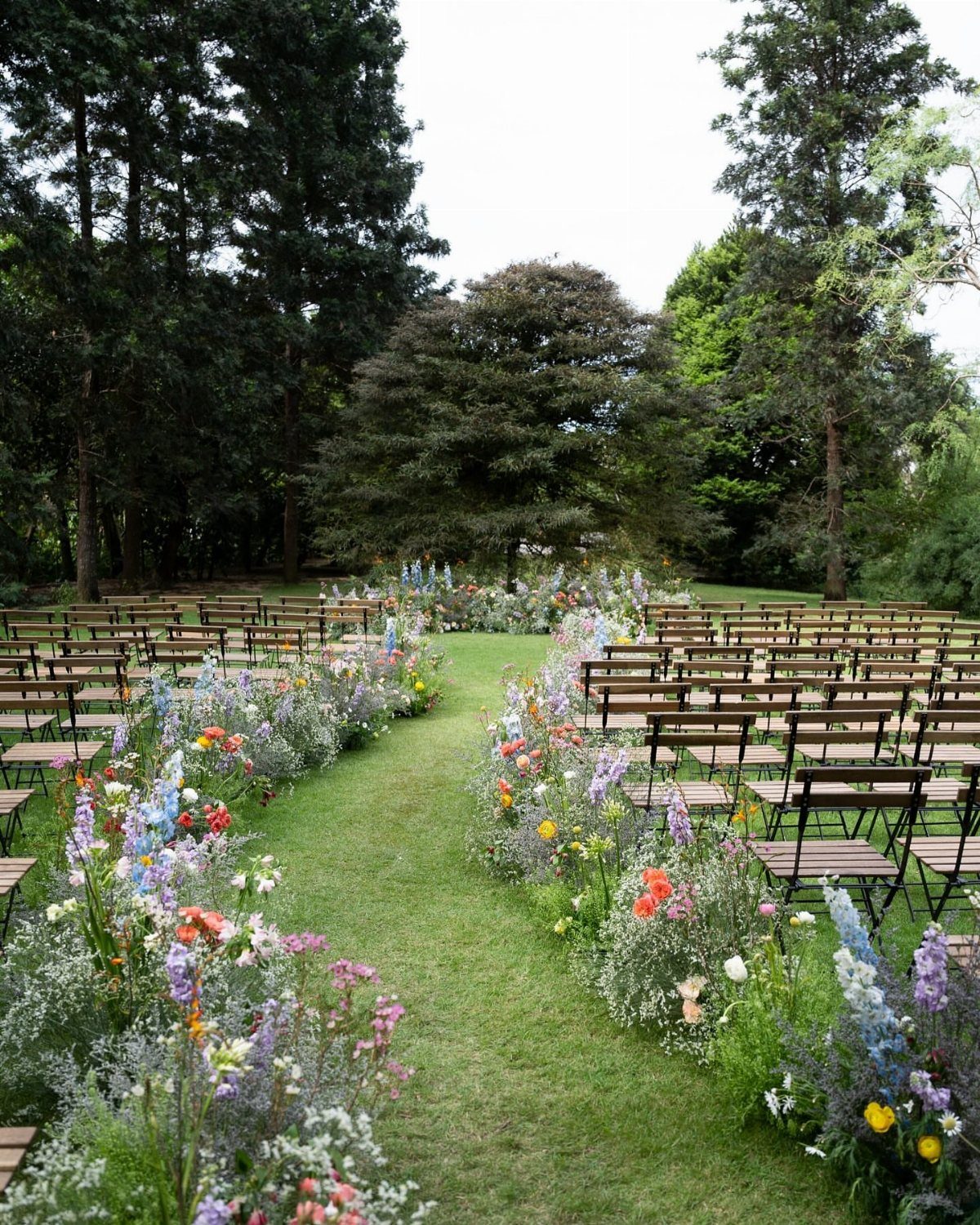 Colorful wildflower arrangements lining a grassy wedding aisle between rows of wooden chairs.