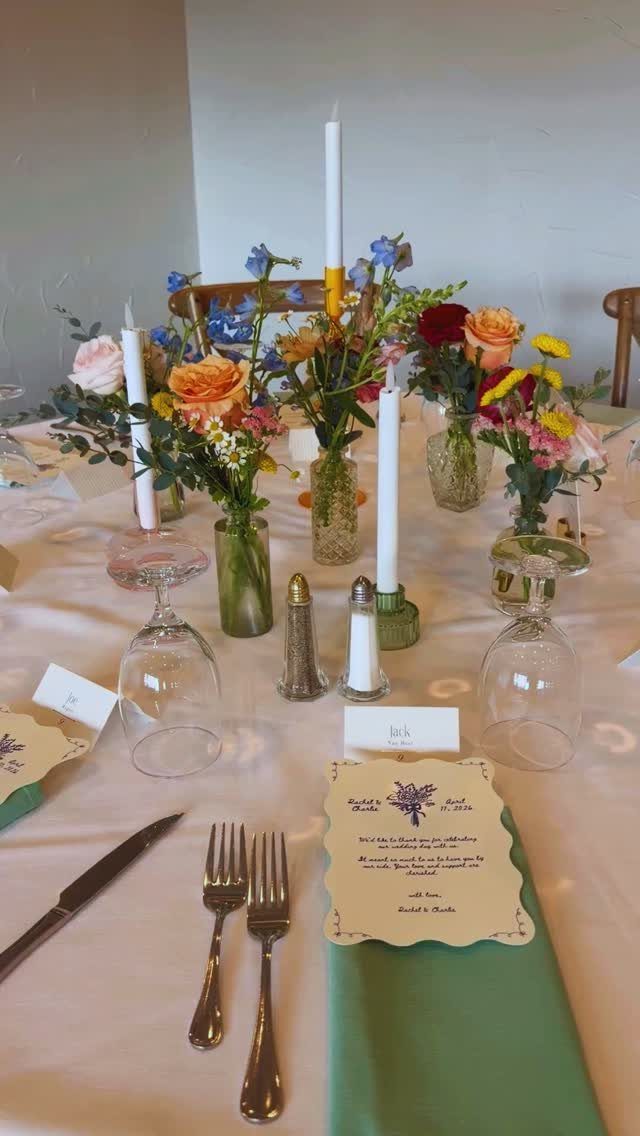 Wildflower centerpieces in small glass vases on a decorated wedding table with candles.