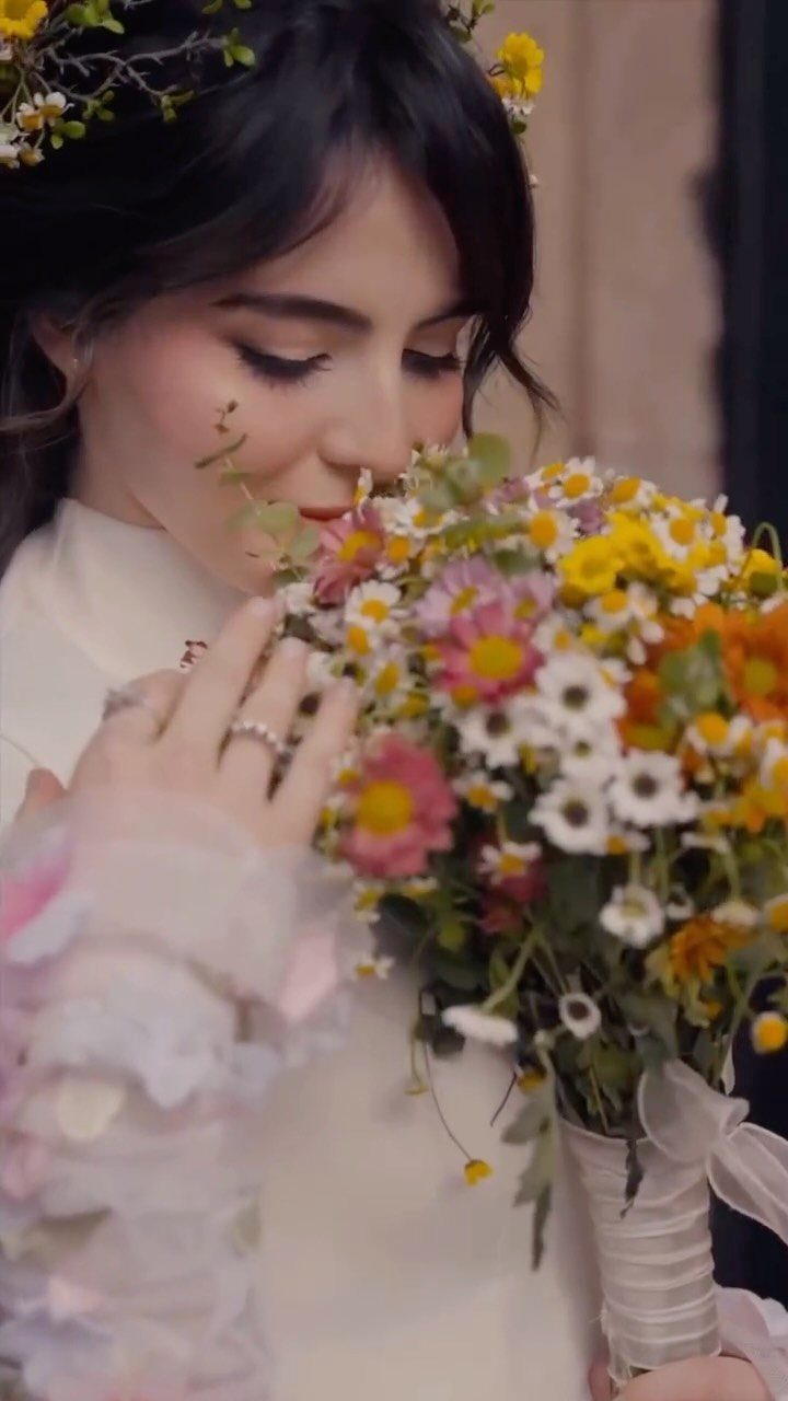 Woman in white dress with floral crown smelling a colorful wildflower wedding bouquet