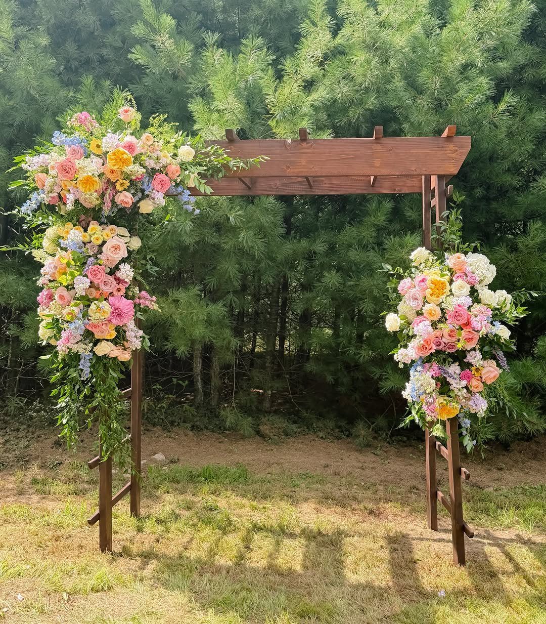 Wooden wedding arch adorned with colorful wildflower arrangements in a forest setting