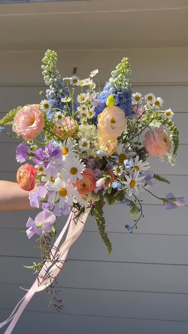 Wildflower wedding bouquet with pink, blue, and white flowers tied with pink ribbon.