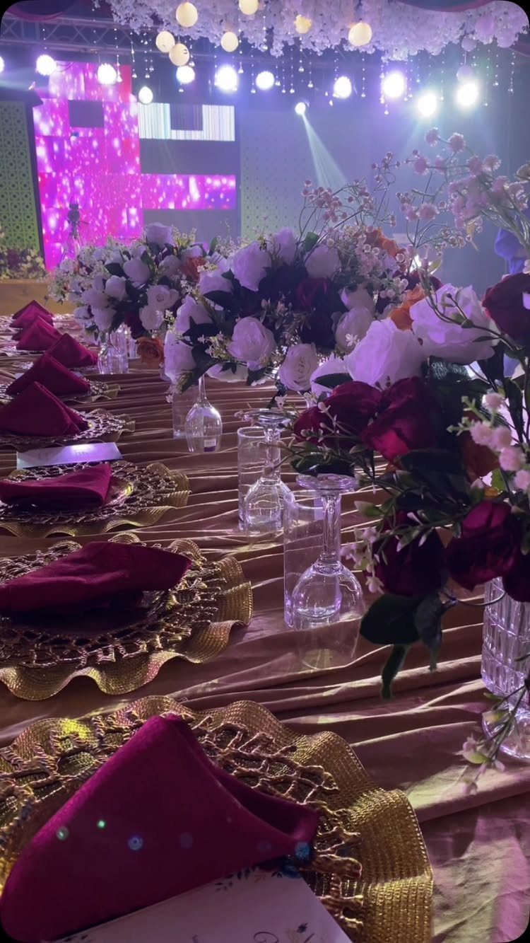 Wedding table setting with burgundy napkins, gold chargers, and red and white roses.