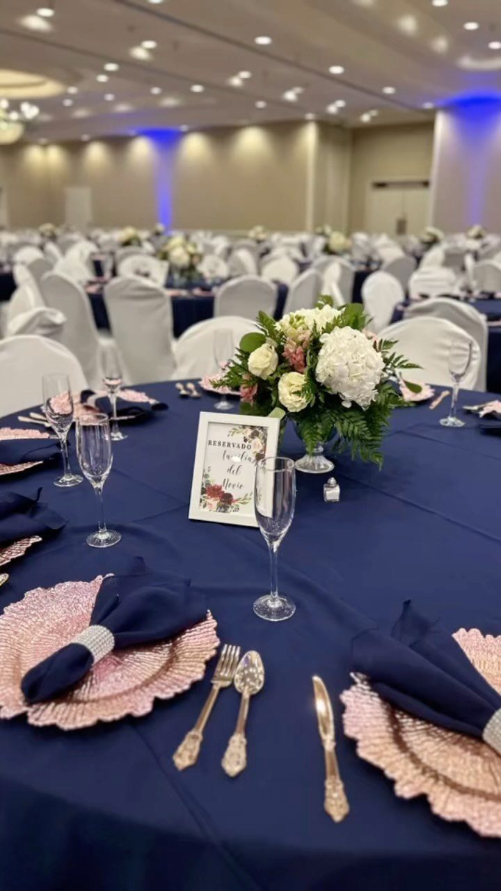 Navy blue wedding table setting with rose gold plates and white floral centerpieces.