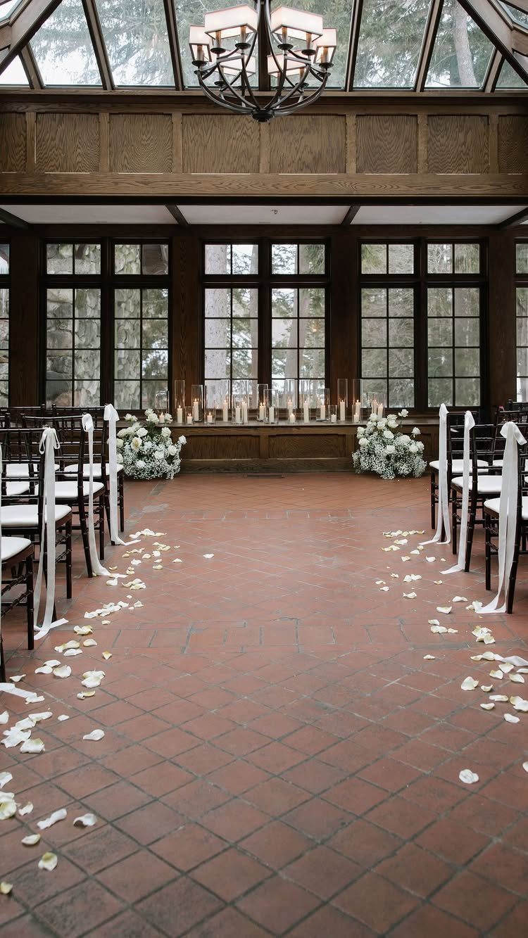 Indoor wedding ceremony setup with white floral arrangements, candles, and white petals.