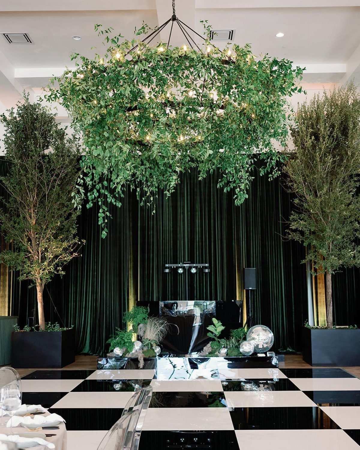 Green foliage chandelier with lights hanging over a checkered dance floor and green curtains.