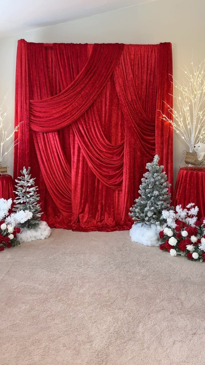 Red velvet backdrop with frosted miniature pine trees and white floral arrangements.