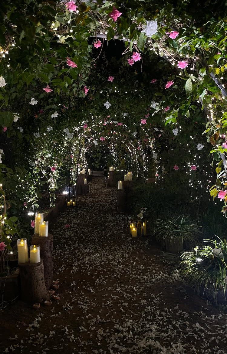 Garden path under a floral arch with fairy lights and pillar candles.